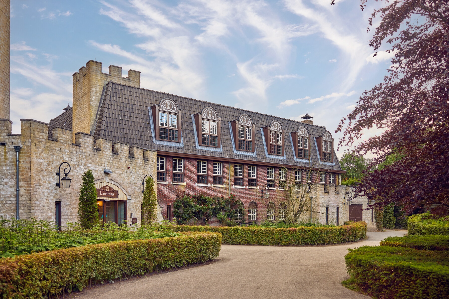 Het Landhuys van Efteling Bosrijk ligt tussen groene hagen en bomen onder een blauwe lucht.