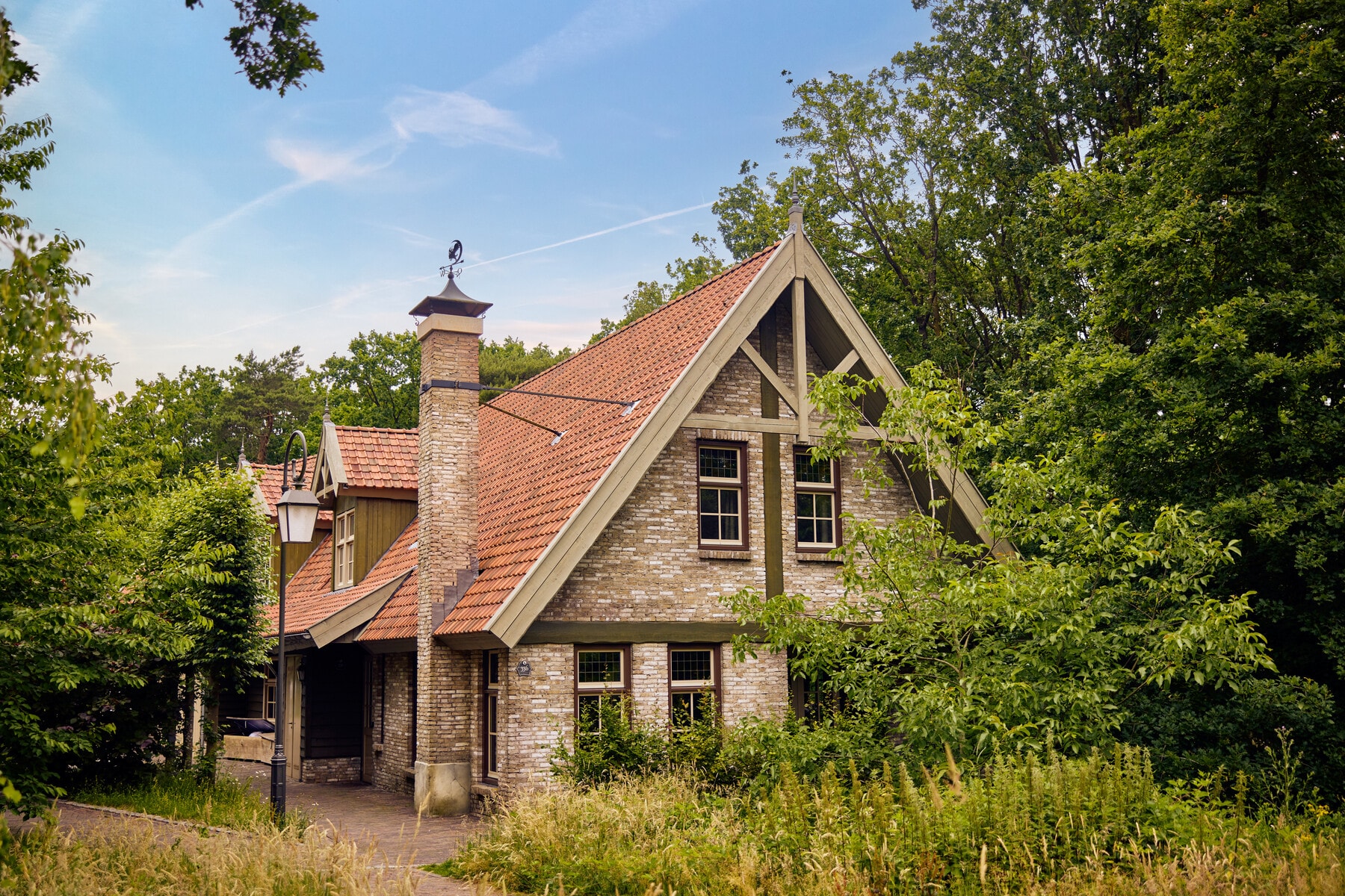 Een Boshoeve van Efteling Bosrijk staat tussen weelderig groen en hoge bomen onder een blauwe lucht.
