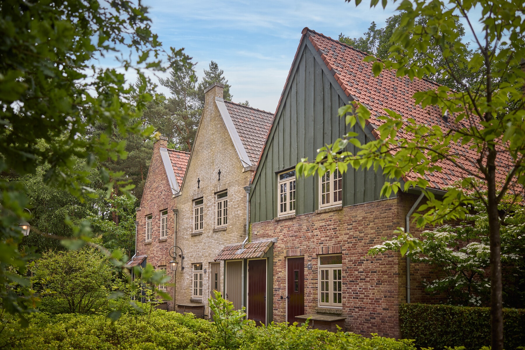 Een 8-persoons Dorpshuys van Efteling Bosrijk staat tussen groene hagen en bomen met karakteristieke gevels.