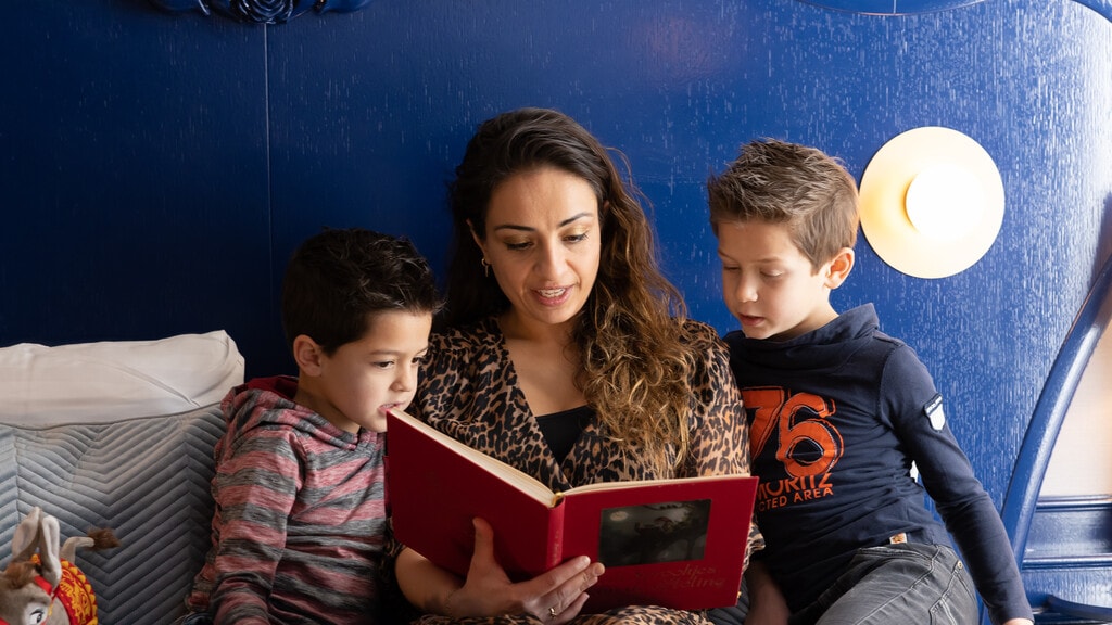 Moeder leest in een suite het Sprookjesboek voor op bed aan haar twee kinderen