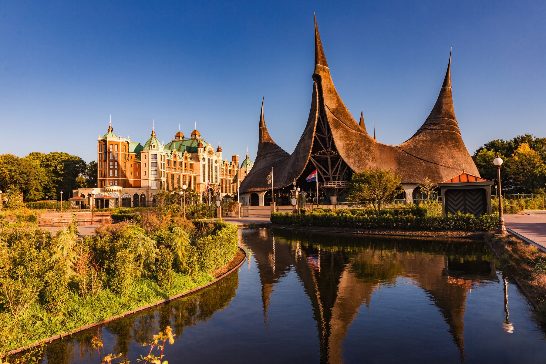 Overzicht van het Huis van de vijf Zintuigen met de vijver ervoor en links het Efteling Grand Hotel tijdens zonsondergang.