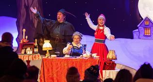 Personnages Efteling Le Petit Chaperon Rouge, Grand-mère et le Chasseur jouent au bingo sur une scène éclairée.