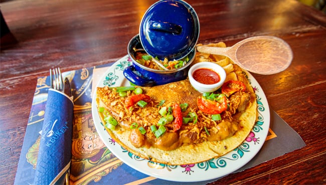 Hartige chef ‘s special van Polles Keuken: saté pannenkoek met atjar, gedroogde uitjes, kroepoek en bosui (€ 13,-).