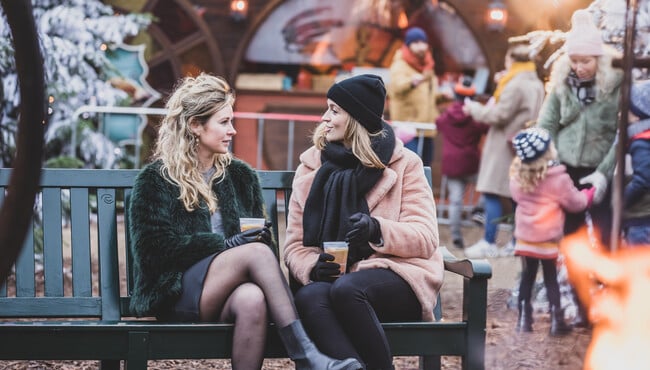 Vriendinnen drinken gluhwein op een bankje op de Warme Winter Weide