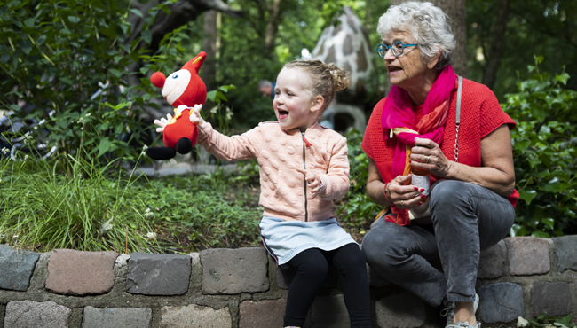 Een oma met haar kleinkind in het Sprookjesbos. Het kleinkind heeft een knuffel van Jokie in haar hand.