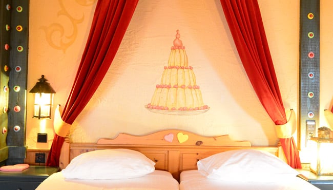 Boven het bed hangt een gordijntje en staat een taart op de muur.