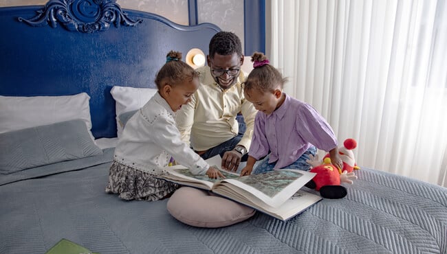 Vader en twee dochters lezen een boek op bed in het Efteling Wonder Hotel.