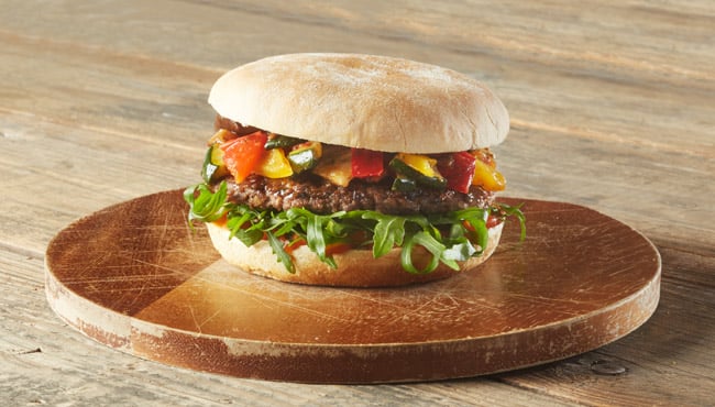 Gegrilde runderburger op een rustiek broodje met paprikaspread, rucola en gegrilde groenten.