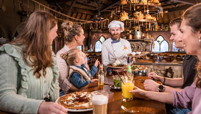 Medewerker van een restaurant serveert pannenkoeken aan gasten aan tafel.