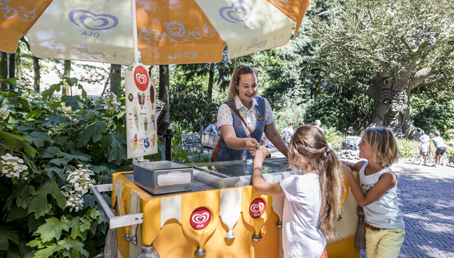 Een medewerker van de Efteling geeft ijsjes aan twee kinderen.