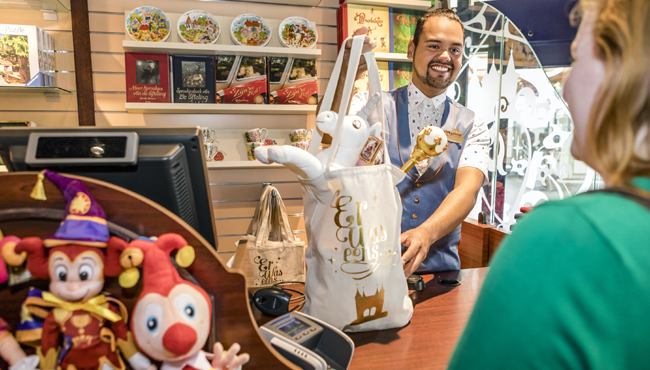Een Efteling-medewerker overhandigd een tas vol souvenirs aan een gast.