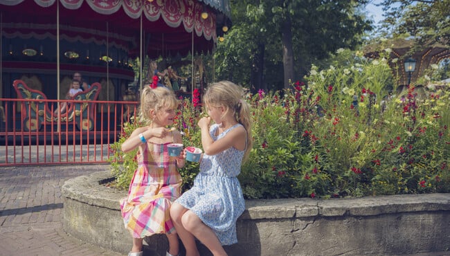 Twee meisjes die een ijsje eten voor een draaimolen op het Anton Pieck Plein. 