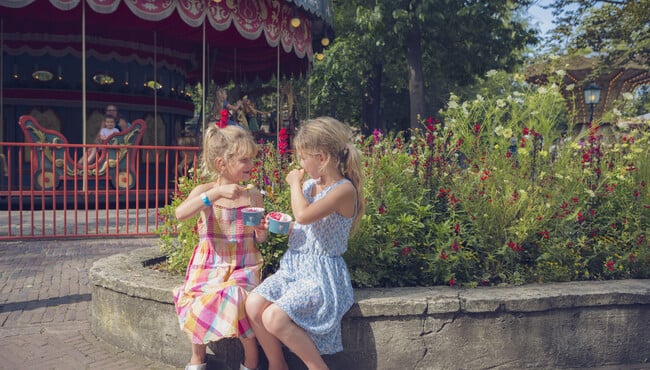 Twee meisjes die een ijsje eten voor een draaimolen op het Anton Pieck Plein.
